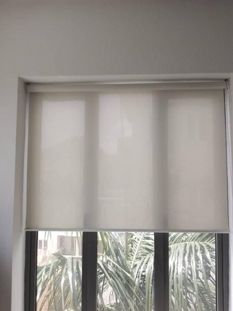 Cream sunscreen roller blind half-lowered over a window, fabric hanging flat and even