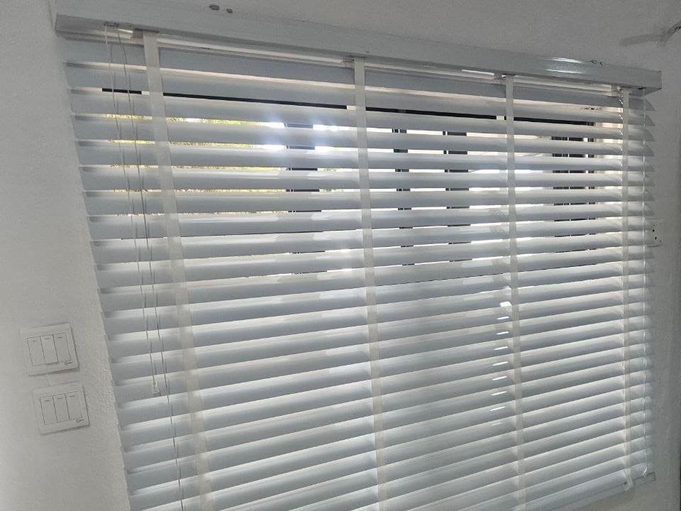 White venetian blind fitted across a wide window, slats tilted to let daylight through while keeping the view screened